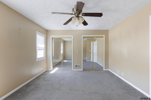 unfurnished bedroom featuring visible vents, carpet floors, two closets, baseboards, and a textured ceiling