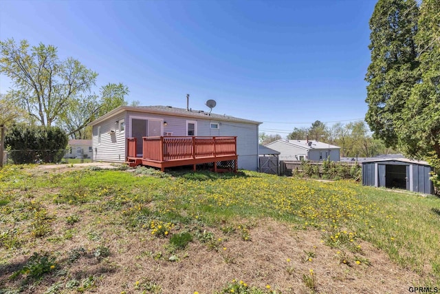 rear view of property featuring an outdoor structure, fence, a wooden deck, and a shed