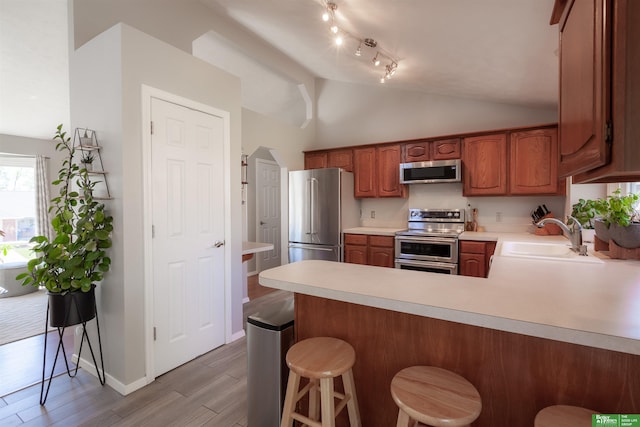 kitchen with a sink, light wood-style floors, light countertops, stainless steel appliances, and lofted ceiling