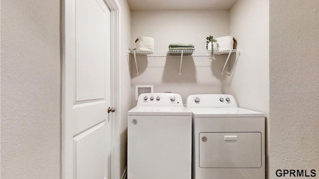 clothes washing area featuring a textured wall, laundry area, and washing machine and dryer