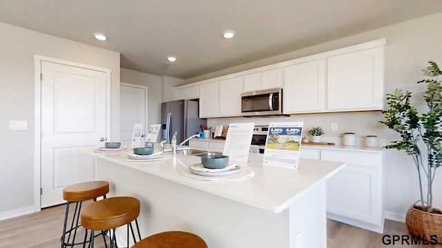 kitchen with white cabinets, appliances with stainless steel finishes, a breakfast bar, and light wood finished floors