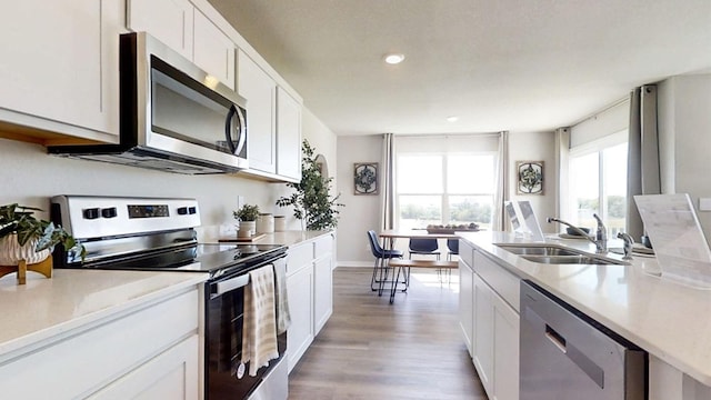 kitchen with white cabinets, stainless steel appliances, a sink, and light wood finished floors