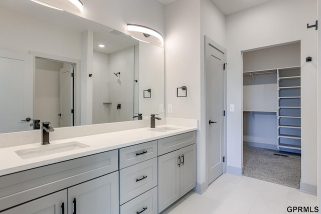 bathroom with tiled shower, a walk in closet, double vanity, and baseboards