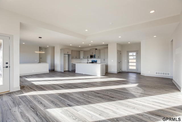 unfurnished living room with light wood-type flooring, baseboards, a sink, and recessed lighting