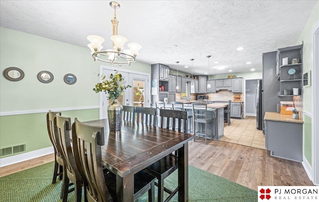 dining room with visible vents, a textured ceiling, light wood-style floors, and a notable chandelier