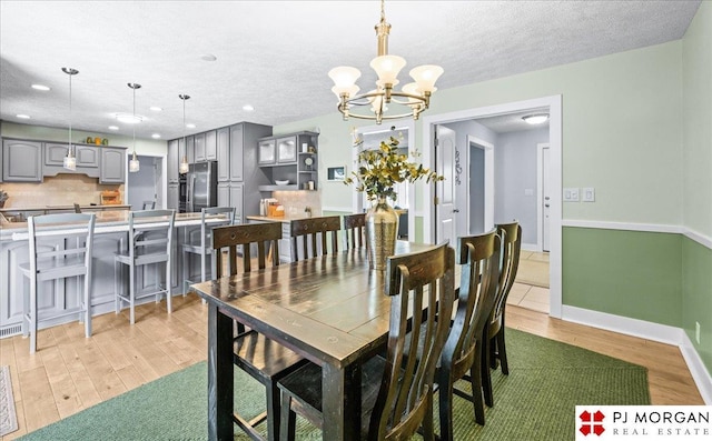 dining space featuring baseboards, recessed lighting, a textured ceiling, light wood-style flooring, and a notable chandelier
