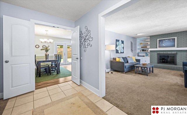 carpeted living area with a textured ceiling, a fireplace, tile patterned floors, baseboards, and a chandelier