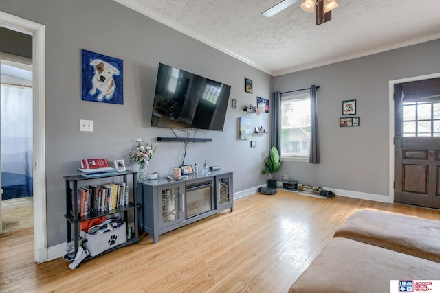 living room with ceiling fan, a textured ceiling, wood finished floors, baseboards, and ornamental molding
