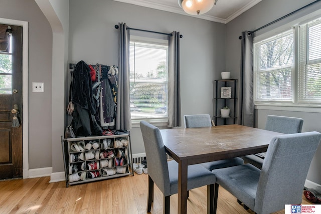 dining space featuring baseboards, ornamental molding, arched walkways, and wood finished floors