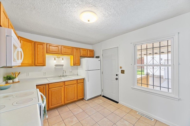 kitchen with light tile patterned flooring, a sink, white appliances, light countertops, and visible vents
