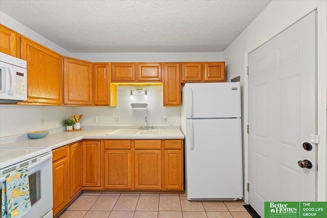 kitchen featuring white appliances, light tile patterned floors, a sink, and light countertops