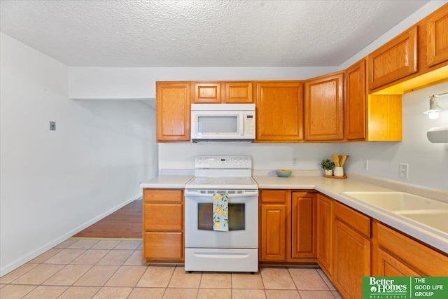 kitchen featuring light tile patterned floors, light countertops, brown cabinetry, and white appliances
