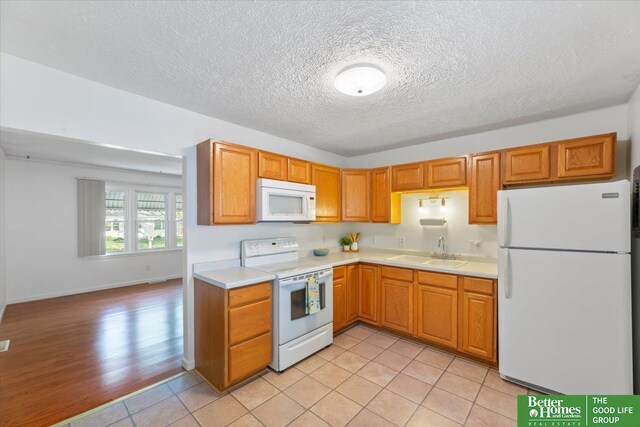 kitchen with light tile patterned flooring, a sink, white appliances, light countertops, and a textured ceiling