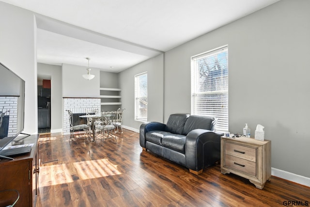 living area featuring a brick fireplace, dark wood-style flooring, baseboards, and built in shelves