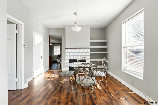 dining space with a brick fireplace, a healthy amount of sunlight, and wood finished floors