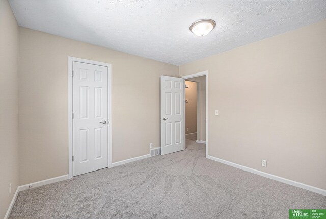 unfurnished bedroom with carpet floors, a textured ceiling, baseboards, and visible vents