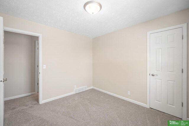 unfurnished bedroom featuring a textured ceiling, baseboards, visible vents, and carpet