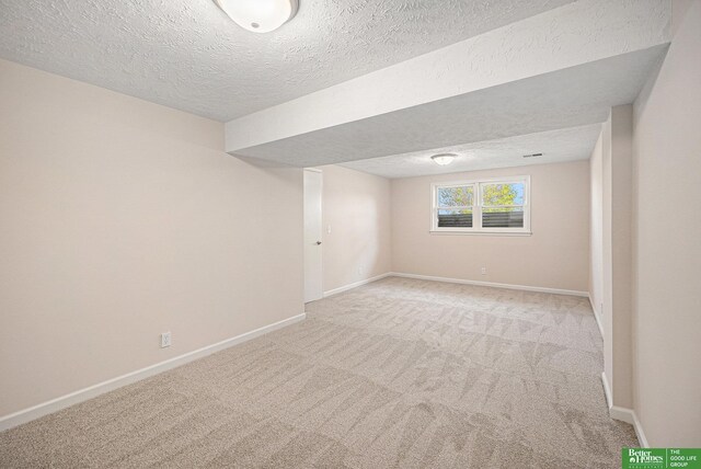 basement featuring baseboards, a textured ceiling, and light colored carpet