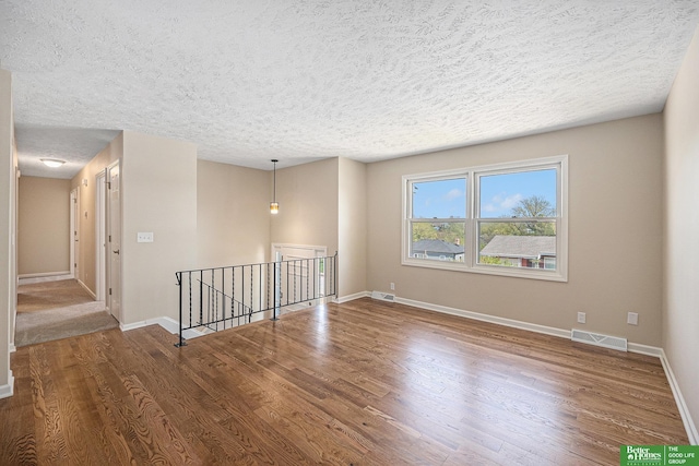 spare room with a textured ceiling, baseboards, wood finished floors, and visible vents