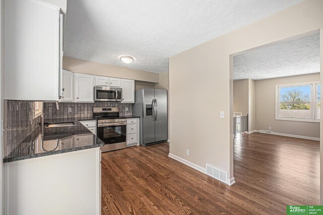 kitchen with appliances with stainless steel finishes, a sink, a textured ceiling, visible vents, and dark wood-style floors