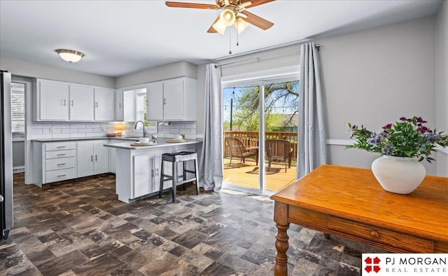 kitchen with a sink, plenty of natural light, a ceiling fan, a peninsula, and backsplash