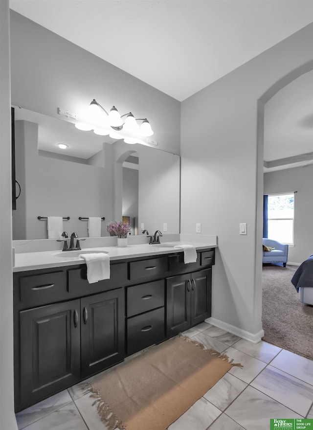 ensuite bathroom with a sink, double vanity, marble finish floor, baseboards, and ensuite bathroom