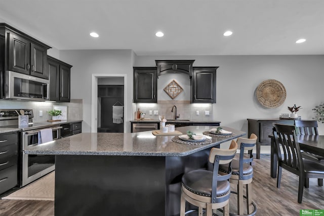 kitchen featuring wood finished floors, a kitchen breakfast bar, a center island, tasteful backsplash, and appliances with stainless steel finishes