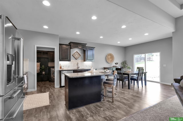 kitchen with appliances with stainless steel finishes, a sink, washer / dryer, a kitchen island, and dark wood-style floors