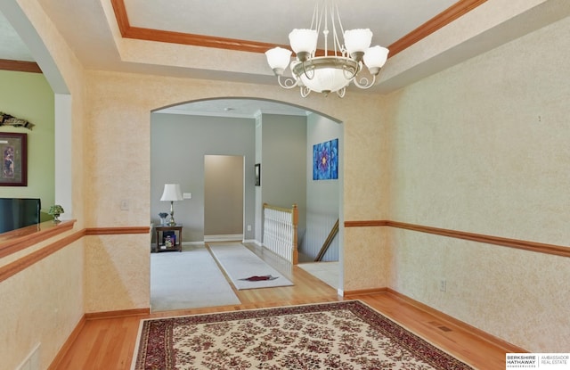 11402 Todd Dr, Blair, NE 68008 - hallway with arched walkways, wood finished floors, ornamental molding, a chandelier, and a tray ceiling
