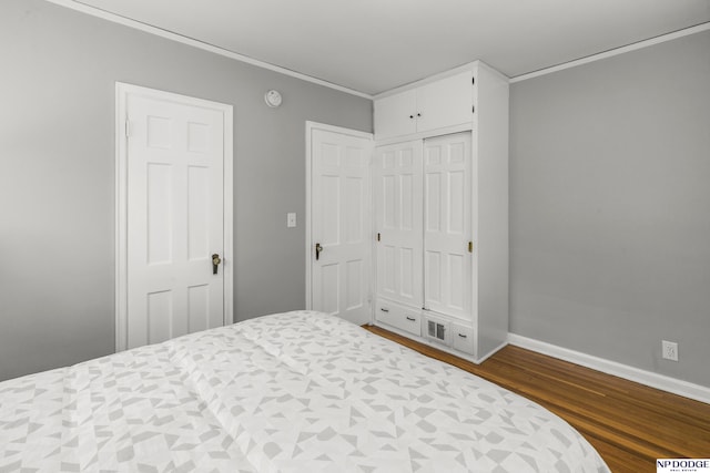 bedroom with crown molding, baseboards, dark wood finished floors, and a closet