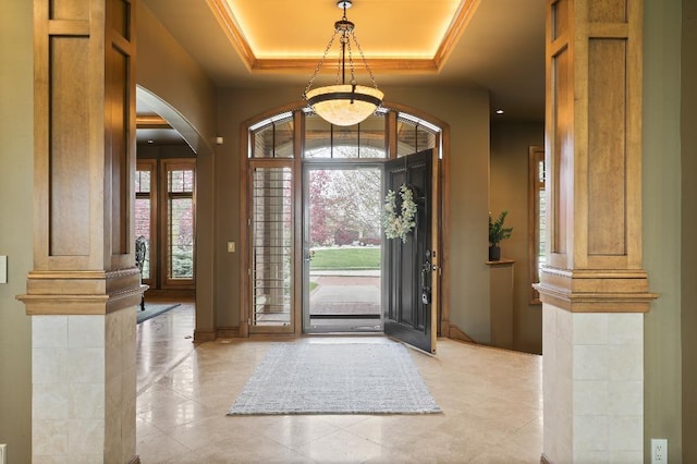 foyer featuring baseboards, ornate columns, a chandelier, a tray ceiling, and arched walkways