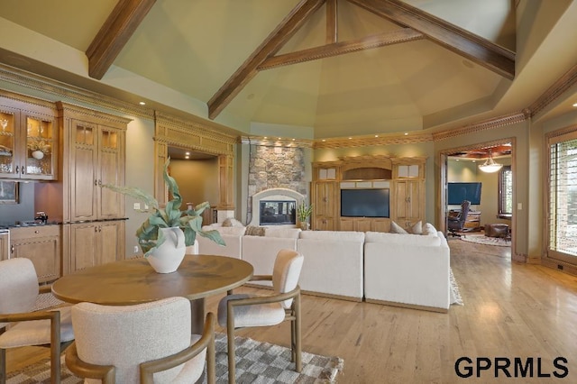 dining space with high vaulted ceiling, beam ceiling, a stone fireplace, and light wood-style flooring