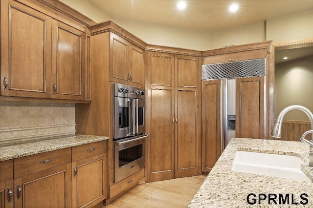 kitchen with paneled built in fridge, brown cabinets, stainless steel double oven, and a sink