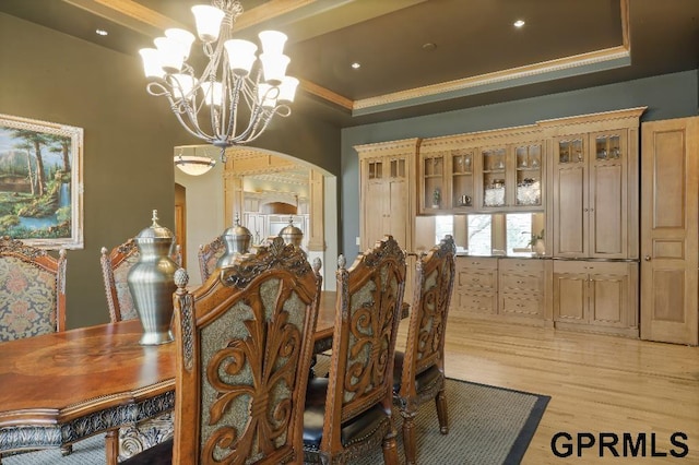 dining room with crown molding, light wood-style floors, a raised ceiling, a chandelier, and arched walkways