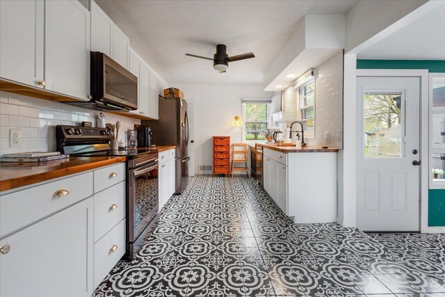kitchen featuring ceiling fan, butcher block countertops, stainless steel appliances, white cabinetry, and backsplash