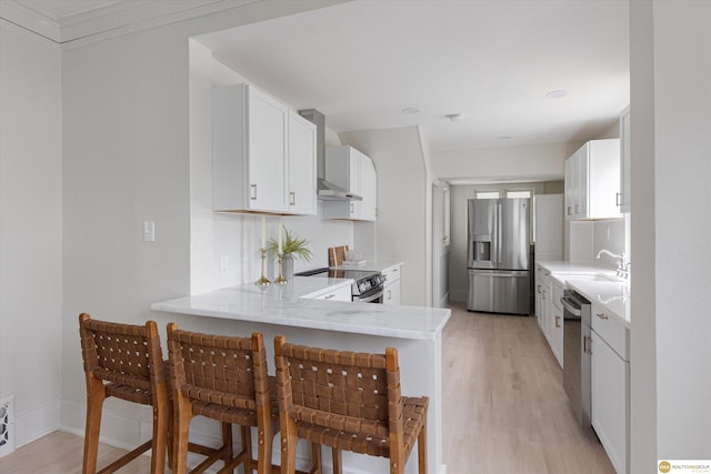 kitchen featuring appliances with stainless steel finishes, a sink, light wood-style floors, white cabinetry, and a peninsula