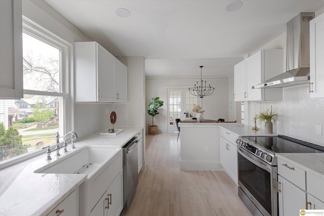 kitchen featuring tasteful backsplash, light wood finished floors, a notable chandelier, stainless steel appliances, and wall chimney exhaust hood