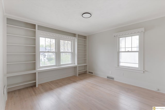 empty room featuring baseboards, visible vents, built in shelves, and wood finished floors