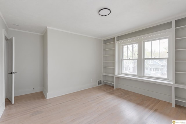 empty room with crown molding, built in shelves, baseboards, light wood-type flooring, and visible vents