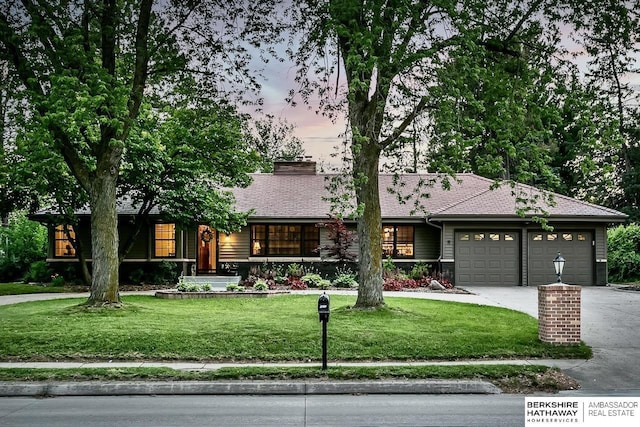 view of front facade featuring an attached garage, concrete driveway, a yard, and roof with shingles