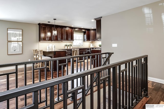 kitchen featuring dark brown cabinets, a sink, dark wood-style floors, dishwasher, and baseboards