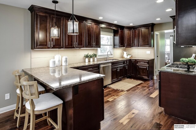 kitchen featuring a sink, stainless steel dishwasher, dark brown cabinetry, a peninsula, and backsplash