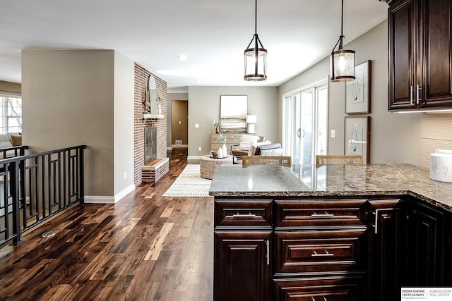 kitchen with a peninsula, a brick fireplace, open floor plan, and dark wood-type flooring