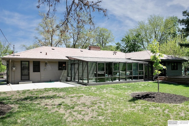 back of house featuring a sunroom, a patio area, a chimney, a yard, and a shingled roof