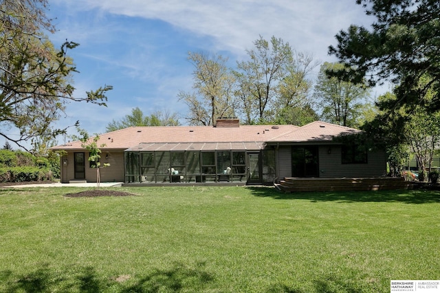 rear view of property featuring a sunroom, a patio area, a chimney, and a lawn