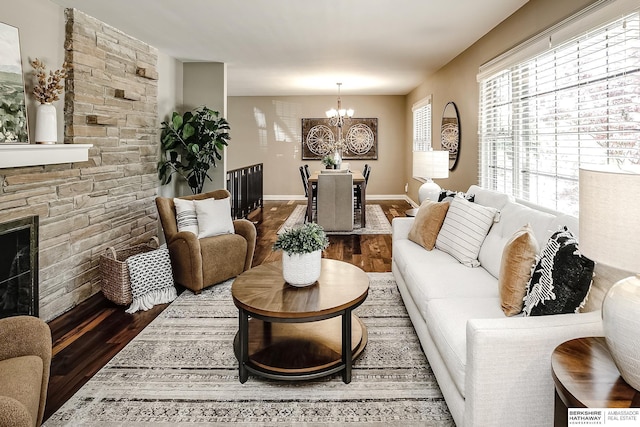 living room featuring baseboards, a notable chandelier, a fireplace, and wood finished floors