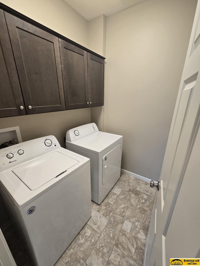 clothes washing area with cabinet space, baseboards, stone finish floor, and washer and clothes dryer