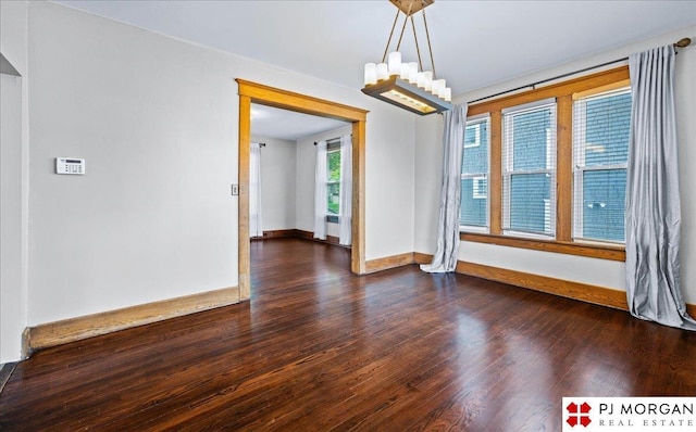 unfurnished room featuring dark wood-type flooring, baseboards, and a chandelier