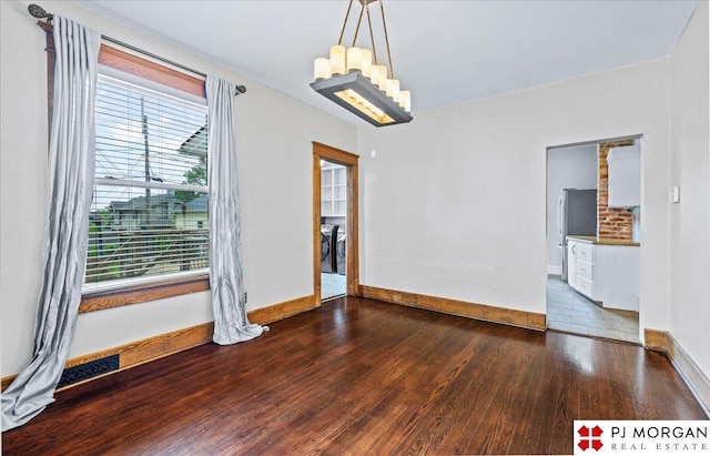 spare room featuring wood finished floors, a chandelier, and baseboards