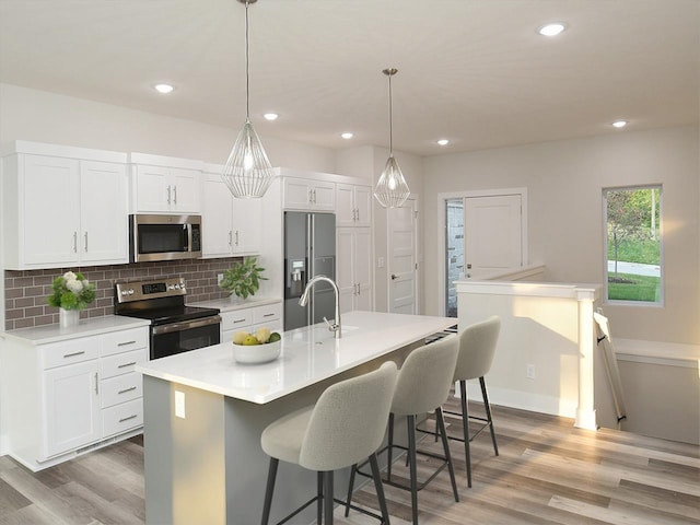 kitchen with a kitchen island with sink, backsplash, appliances with stainless steel finishes, light wood finished floors, and white cabinetry